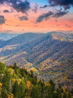 the mountains are covered in autumn foliage and trees with colorful leaves on them as the sun sets