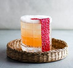 a glass filled with liquid sitting on top of a wicker tray next to a bottle