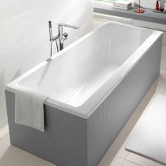 a white bath tub sitting on top of a tiled floor next to a red chair