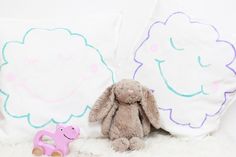 two stuffed animals sitting next to each other on a white bed with pink and blue pillows