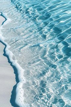 an ocean wave is coming in to the shore line with white sand and blue water