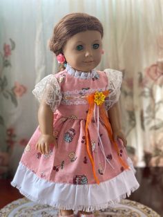 the doll is wearing a pink dress with white ruffles and an orange bow