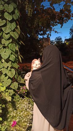 a woman in a black shawl holding a white and brown cat on her back