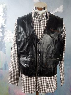 "This Swedish vintage black leather motorcycle vest has a V neckline, and closes in the front with four silvery black snap buttons. The brand name Halvarssons is embroidered on the left chest, and the handsome genuine leather waistcoat has two buttoned pockets on the front. Each lower side has an adjustable leather mini-belt. The back features a stunning embroidered motorcycle tire with the brand name running through the center of it. The vest is fully lined in a beige cotton fabric. Chest = 42 Moto Vest For Biker Events In Fall, Moto Style Vest For Biker Events In Fall, Leather Vest Jacket For Fall Biker Events, Moto Style Black Vest For Biker Events, Biker Vest For Motorcycling In Fall, Sleeveless Black Biker Jacket For Fall, Fall Biker Vest For Motorcycling, Black Rockabilly Biker Jacket For Biker Events, Sleeveless Black Biker Jacket For Biker Events