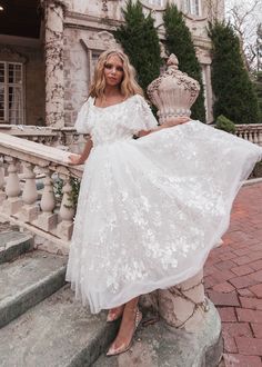 a woman in a white dress is standing on some steps and posing for the camera