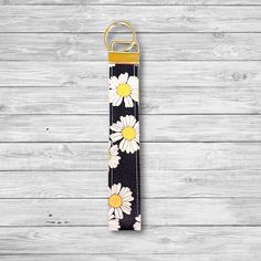 a keychain with daisies on it hanging from a wooden wall next to a pair of scissors