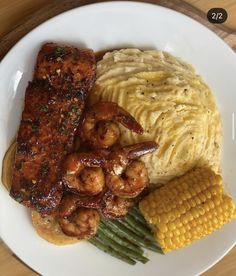 a white plate topped with meat and veggies next to corn on the cob