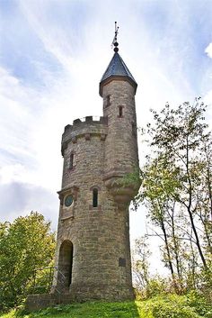 an old stone tower with a clock on it's side in the middle of trees