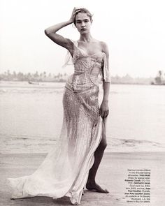 black and white photograph of a woman in a dress standing on the beach with her hands behind her head