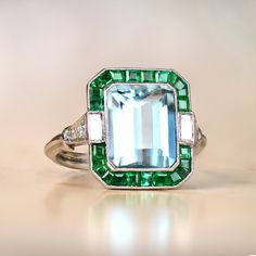 This stunning ring boasts a captivating aquamarine weight of approximately 3.22 carats, with a halo of emeralds and diamonds. The ring shoulders are elegant with diamonds, and its it is meticulously crafted from platinum, featuring an intricate openwork under-gallery. The central aquamarine, while the combined weight of the natural green emerald is approx 0.70 carats. ✦ GEMSTONES  SPECIFICATIONS: Center Gemstone: Aquamarine Aquamarine Weight: Approx 3.22 Carats  Total Emerald Weight: Approx 0.70 Diamond Ring With Halo, Emerald Cut Aquamarine Ring, Ring With Halo, Estate Diamond Jewelry, Emerald Cut Rings, Gemstone Engagement, Baguette Cut Diamond, Aquamarine Rings, Platinum Ring