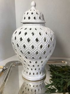 a white vase sitting on top of a table next to a potted green plant