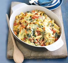 a casserole dish with spinach, tomatoes and cheese on a cutting board