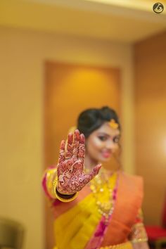 a woman in yellow and orange sari holding her hand up to show the hendi