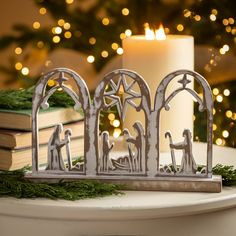 a candle is lit next to a nativity scene on a table with christmas lights in the background