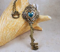 "Victorian skeleton key necklace in bronze. A bronze plated skeleton key has been adorned with stacked layers of filigree and a delicate crystal heart nestled inside a bronze floral heat. Choose your crystal heart color choice at check out. Available colors are: Red Turquoise Blue Amethyst The key has been wrapped with bronze chain and has a tiny charm hanging from the bottom that says \"wish\". Each layer has been carefully sealed with a glossy clear resin to permanently fuse the layers togethe Steampunk Jewelry With Keys For Gifts, Heart Jewlery, Victorian Skeleton, Fantasy Key, Key Necklace Vintage, Large Locket, Saint Helens, Skeleton Key Necklace, Grunge Accessories