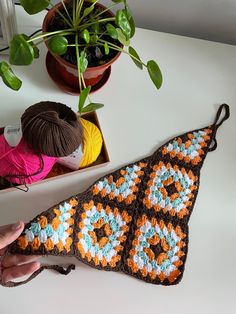 a crocheted triangle is sitting on a table next to a potted plant