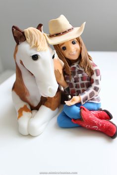 a doll sitting next to a toy horse on top of a white table with a cowboy hat