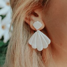 a close up of a person wearing some kind of earring with flowers in the background