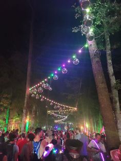 many people are gathered in the park at night with lights and balloons hanging from trees