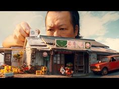 a man holding up a camera in front of a small building with cars parked outside