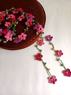 the pink flowers are attached to the brown hat on the white tablecloth and next to it is a string of crocheted beads