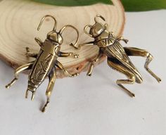 two gold bug figurines sitting on top of a piece of wood