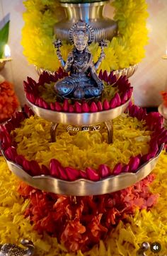 there is a buddha statue on top of the three tiered trays covered in flowers