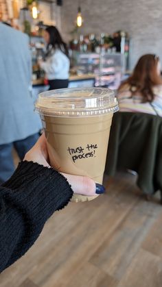 a person holding up a cup with the words trust the process written on it in black ink