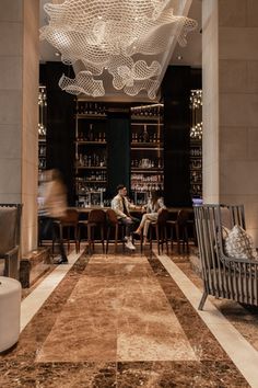 two people sitting at a bar in a hotel lobby with chandeliers hanging from the ceiling