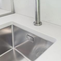 a stainless steel kitchen sink under a faucet in a white countertop area