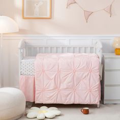 a white crib with pink bedding and pillows on the floor next to it