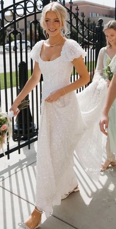 a woman in a white dress standing next to a fence