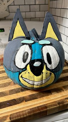 a painted cat pumpkin sitting on top of a wooden cutting board