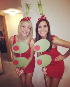 two women in red dresses holding green and red circles on their heads while standing next to each other