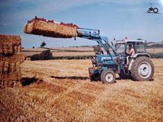 a tractor with hay being loaded onto it's back in the middle of a field