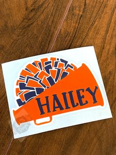 an orange and blue sticker with the word haley on it sitting on a wooden table