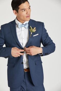 a man in a blue suit is adjusting his bow tie and looking at the camera