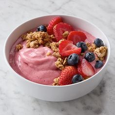 a bowl filled with fruit and granola on top of a marble countertop next to a cup of yogurt