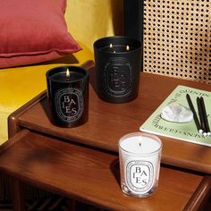 three candles sitting on top of a wooden table next to a book and some pillows