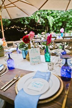 an outdoor table set with place settings, plates and utensils for guests to eat