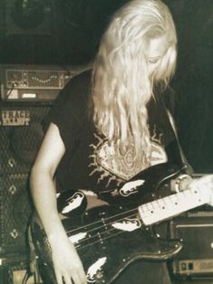 a man with long hair playing a guitar in front of some amps and sound equipment