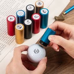 a person is holding a golf ball in front of several colored markers on a table