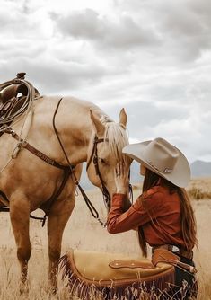 a woman wearing a cowboy hat and sitting on a saddle next to a brown horse