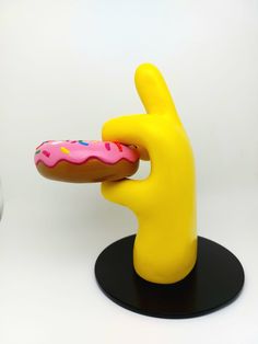 a donut with pink frosting and sprinkles is being held by a yellow hand