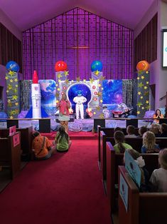 children are sitting on the floor in front of a stage set with balloons and decorations