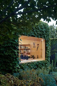 two people are sitting in an open bookcase surrounded by greenery