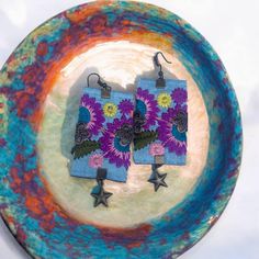 pair of earrings with purple and blue flowers on them sitting on top of a plate