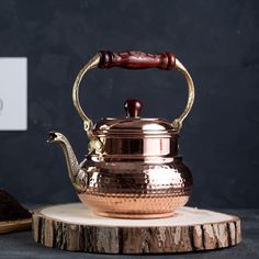 a metal tea pot with a wooden handle and a snake on the side sitting on a piece of wood