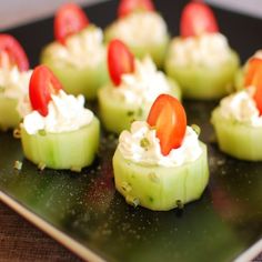 cucumber bites are topped with tomatoes and whipped cream on a black platter