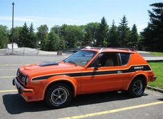 an orange and black car parked in a parking lot next to some trees on a sunny day